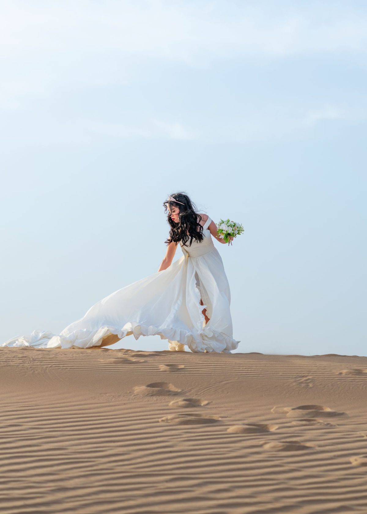 Bride in an elegant gown on desert dunes in Dubai with glamorous makeup